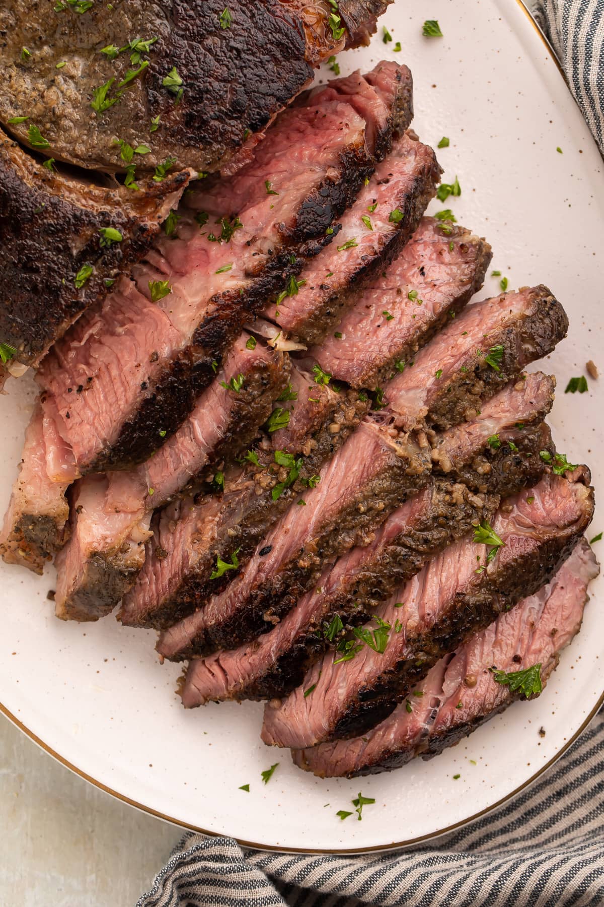 Overhead photo of sous vide chuck roast on a white platter, with half the chuck roast sliced into thin strips and fanned out to show the crust and the inside of the roast.