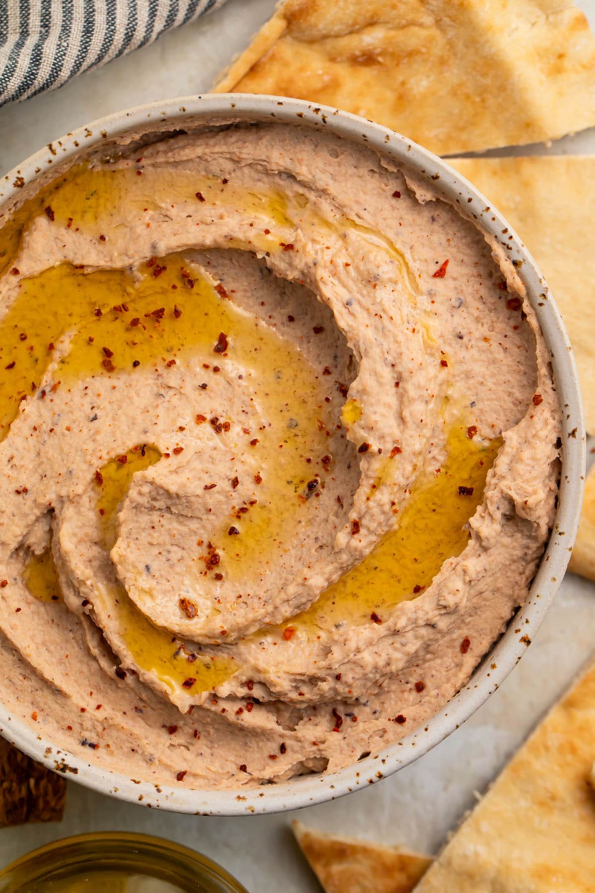 Top-down, close view of a bowl of black eyed pea hummus swirled with olive oil and garnished with fresh herbs.