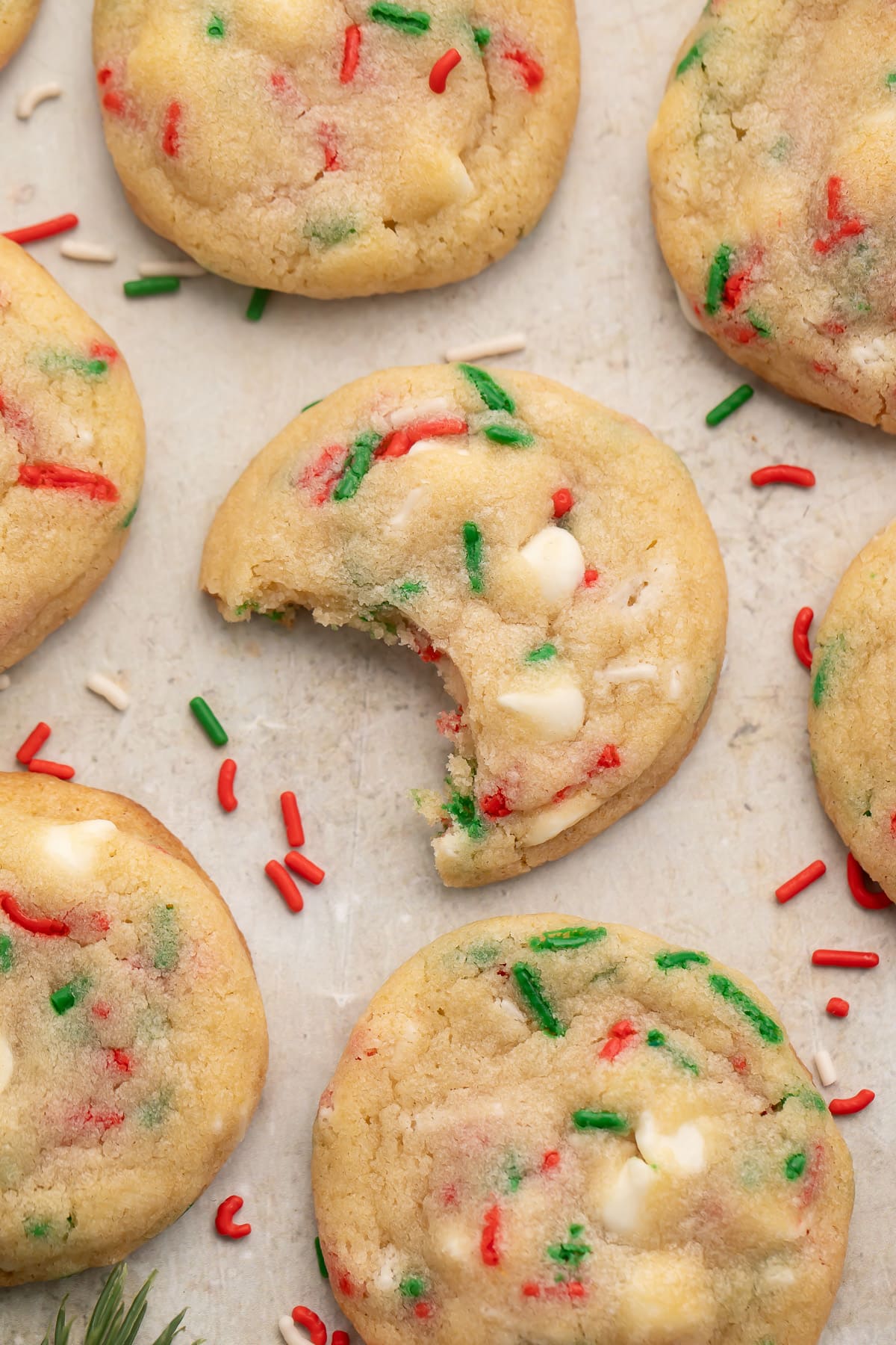 Rows of Christmas confetti cookies on a sheet of parchment paper with red, white, and green sprinkles. The center cookie is missing one bite from the side.