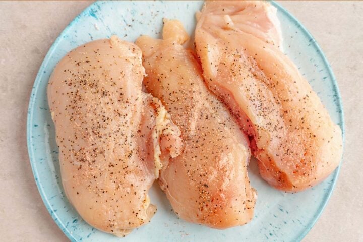 Three large seasoned chicken breasts on a blue plate.