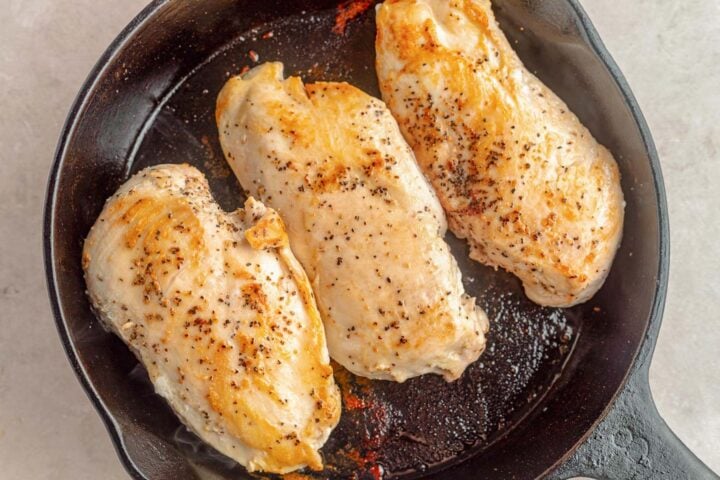 Three large seasoned chicken breasts in a large cast-iron skillet.