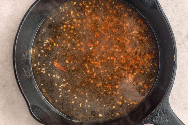 Chicken broth added to minced garlic and olive oil in a large cast-iron skillet.