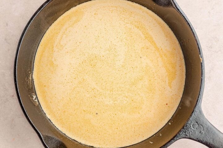 Heavy cream added to chicken broth and minced garlic in a large cast-iron skillet.