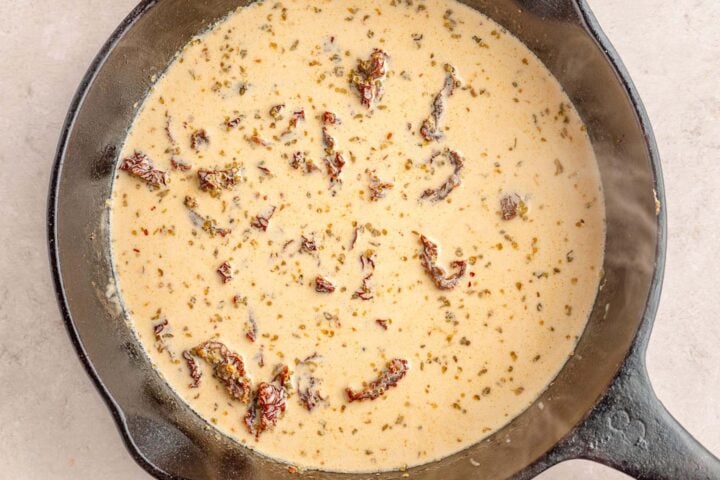 Sun-dried tomatoes and crushed red pepper flakes added to a creamy mixture in a large cast-iron skillet.