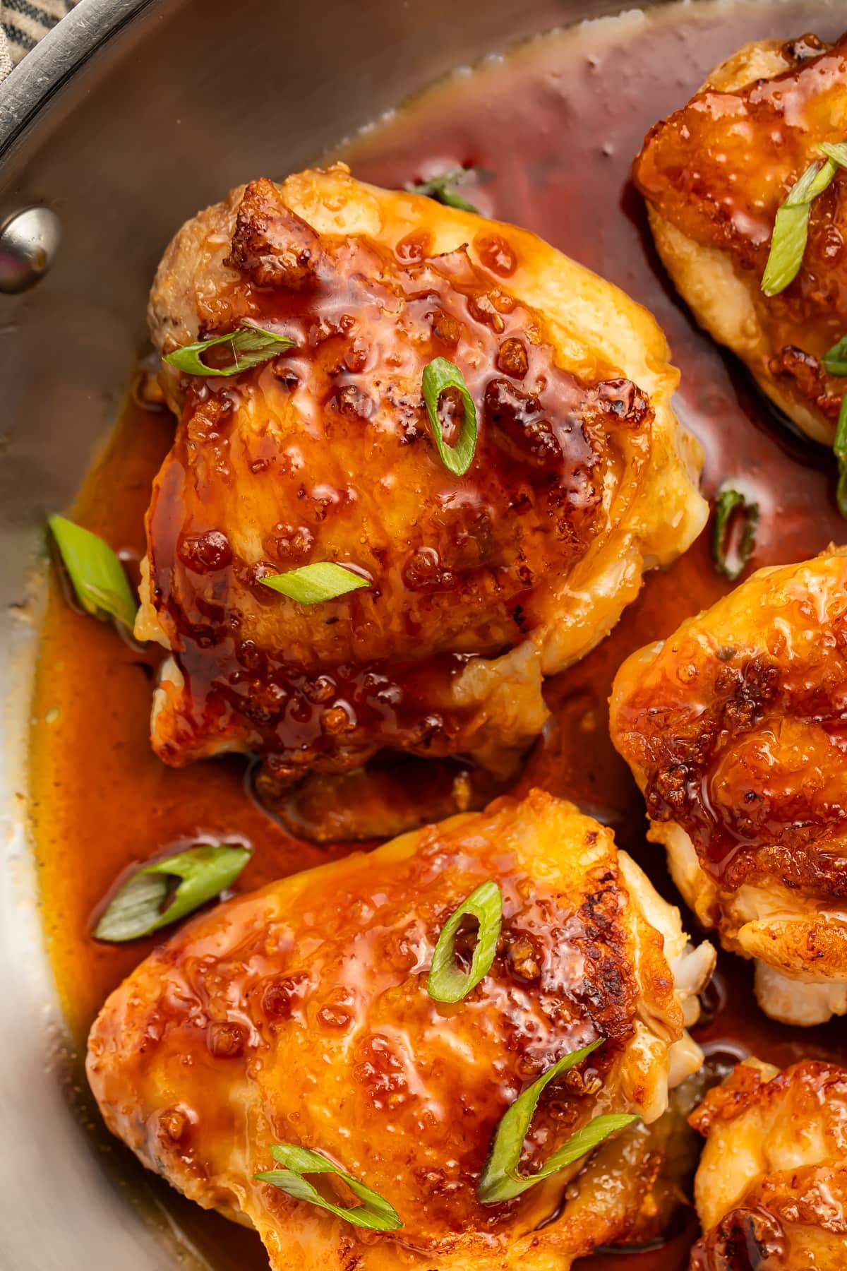 Honey garlic chicken thighs, seared and then roasted until crisp, resting in a silver skillet with additional sauce.
