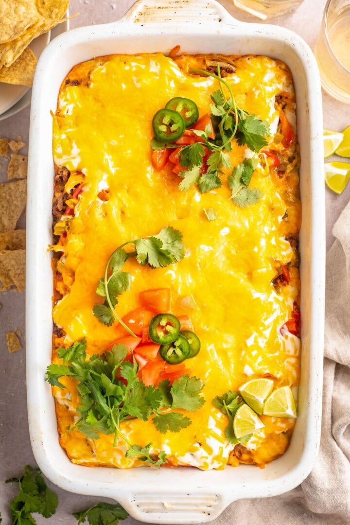 Overhead view of a large white rectangular casserole dish holding John Wayne casserole topped with melted cheese, tomatoes, jalapeño slices, and cilantro.