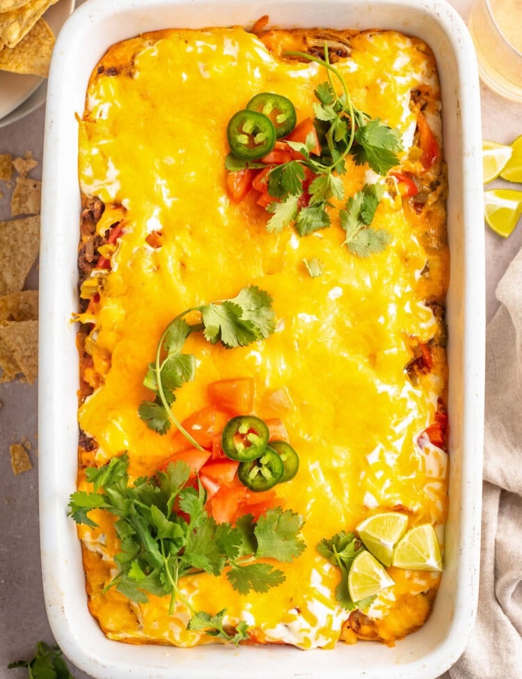 Overhead view of a large white rectangular casserole dish holding John Wayne casserole topped with melted cheese, tomatoes, jalapeño slices, and cilantro.