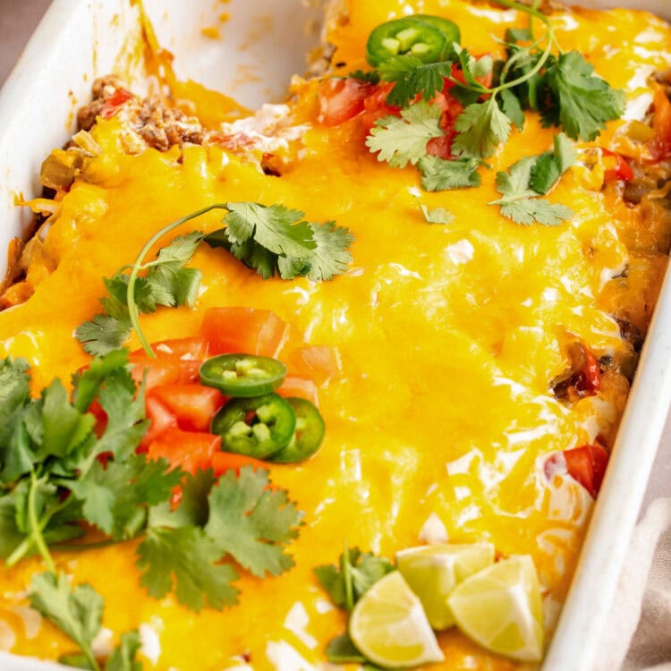 Overhead view of a large white rectangular casserole dish holding John Wayne casserole topped with melted cheese, tomatoes, jalapeño slices, and cilantro.
