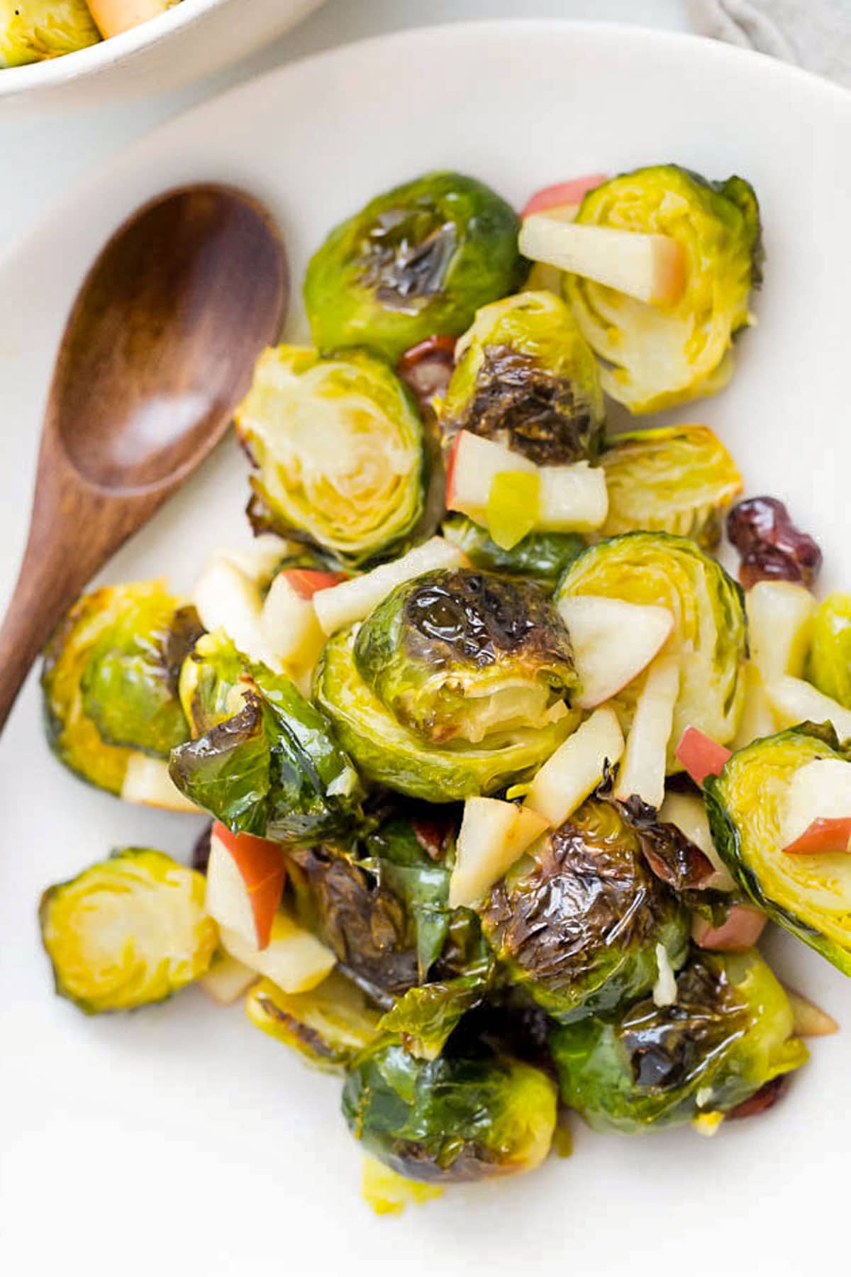 Close-up of Brussels Sprouts salad on a white plate with a wooden spoon.