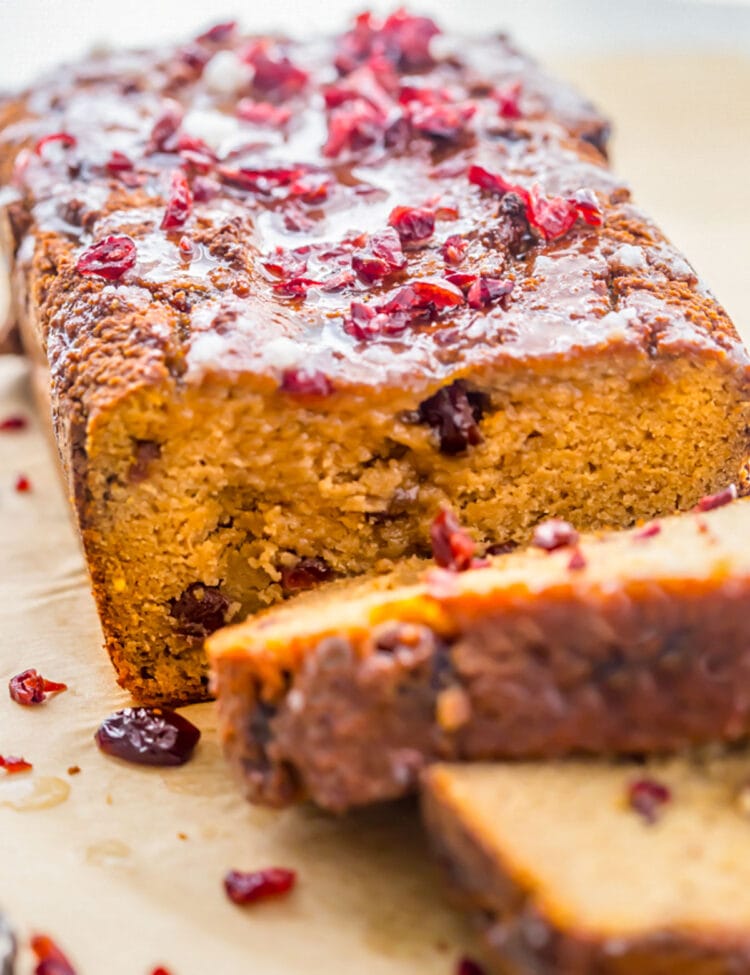Gluten free, grain free, dairy free cranberry orange pound cake on a sheet of parchment paper, with 2 slices removed from the end of the loaf to show the inside of the cake.