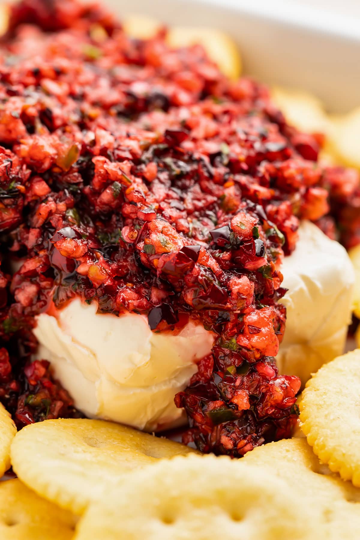 Cranberry salsa piled on top of a block of softened cream cheese, surrounded by buttery round crackers.