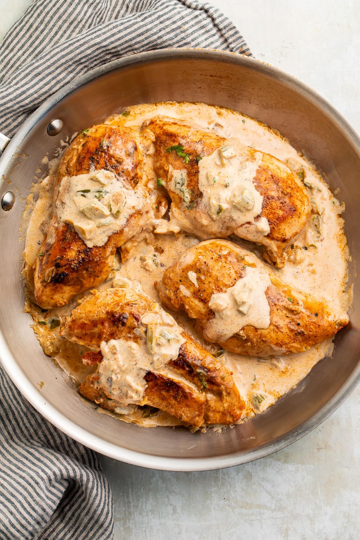 Four seared Cajun-seasoned chicken breasts topped with a creamy sauce in a large silver skillet.