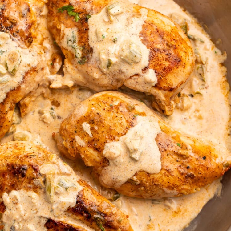 Three seared Cajun-seasoned chicken breasts topped with a creamy sauce in a large silver skillet.