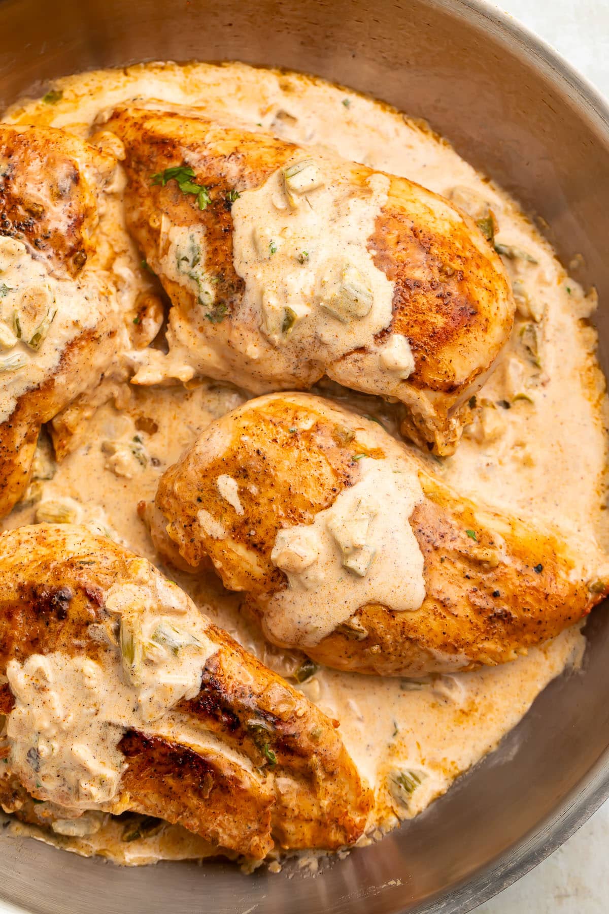 Three seared Cajun-seasoned chicken breasts topped with a creamy sauce in a large silver skillet.