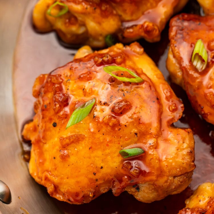 Honey sriracha chicken thighs resting in a large silver skillet with honey sriracha sauce.