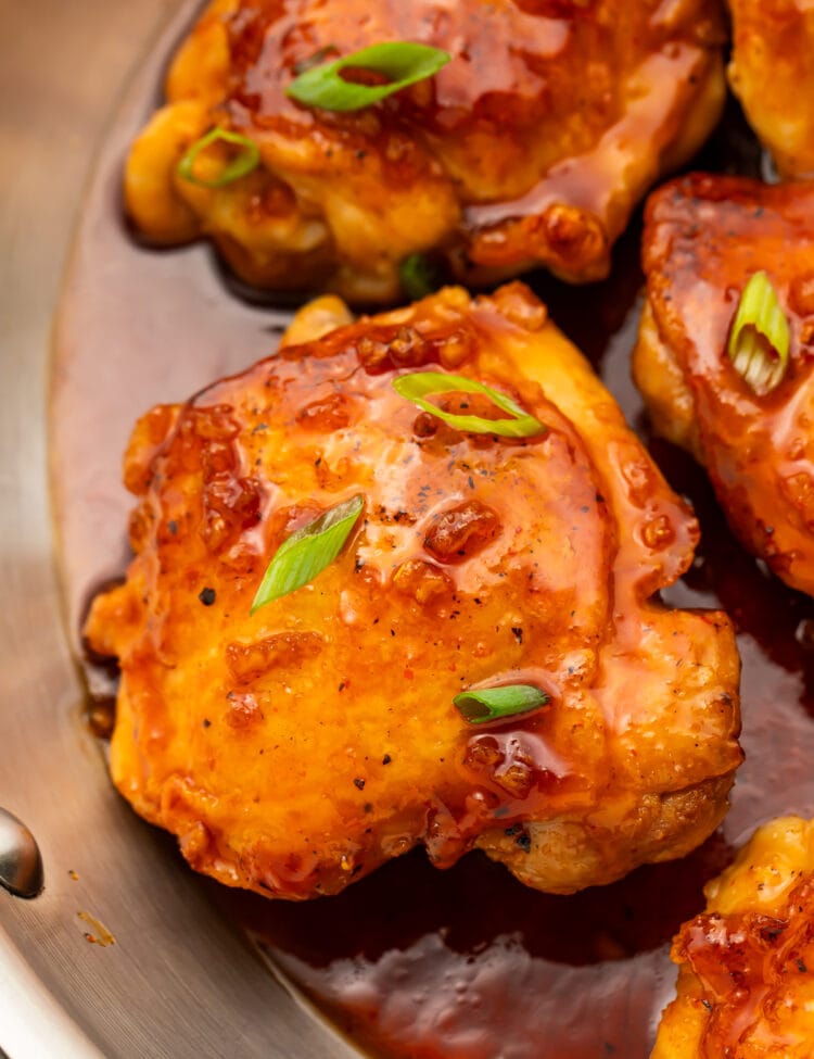 Honey sriracha chicken thighs resting in a large silver skillet with honey sriracha sauce.