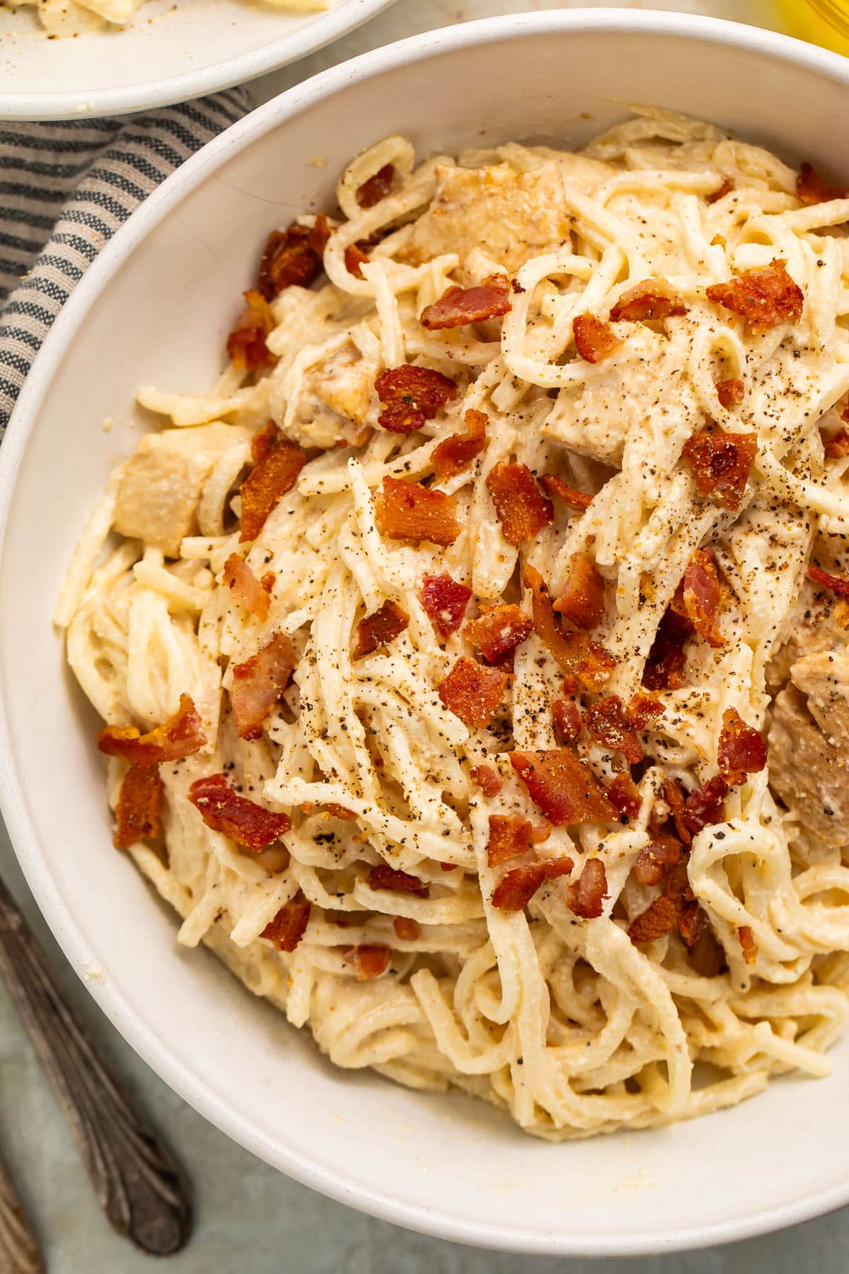 A large white bowl of paleo carbonara made with palmini, dairy-free Alfredo sauce, and compatible bacon.
