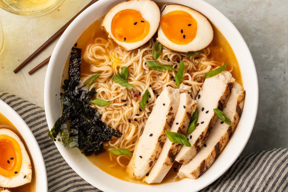 A bowl of 15 minute spicy ramen with jammy eggs and slices of chicken.