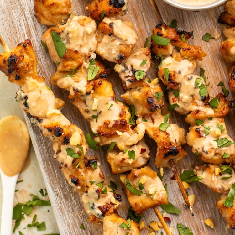 Chicken satay on bamboo skewers resting on a wooden serving board.