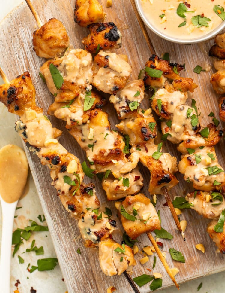 Chicken satay on bamboo skewers resting on a wooden serving board.