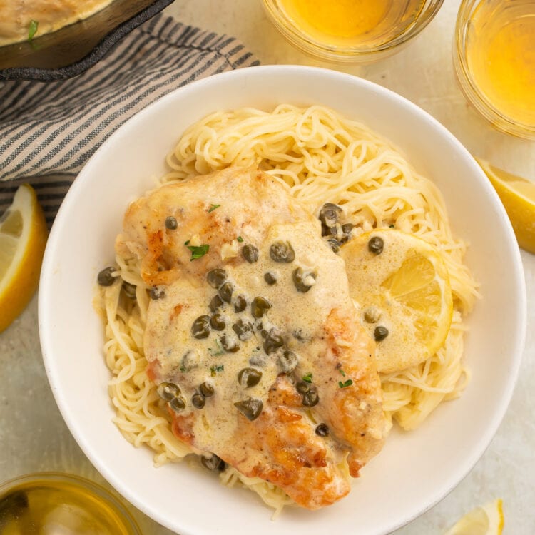 Chicken piccata plated with pasta and capers.