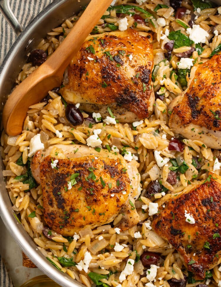 A silver skillet holding Greek seasoned chicken thighs with orzo and feta.