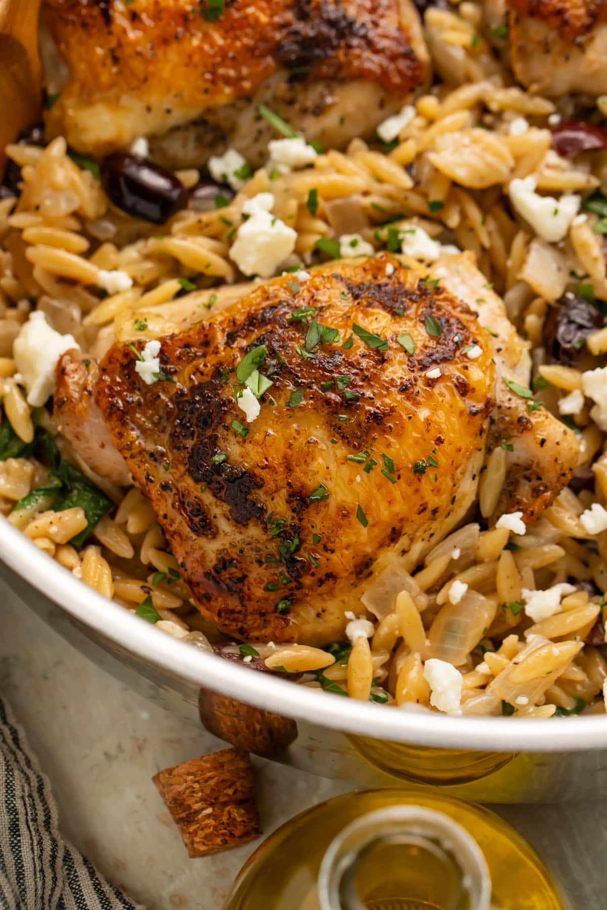 Close-up of a Greek seasoned chicken thigh in a skillet with orzo and feta.