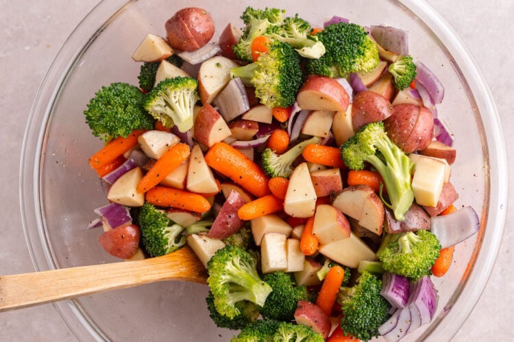 Mixed vegetables in a large glass mixing bowl tossed with oil and salt and pepper.