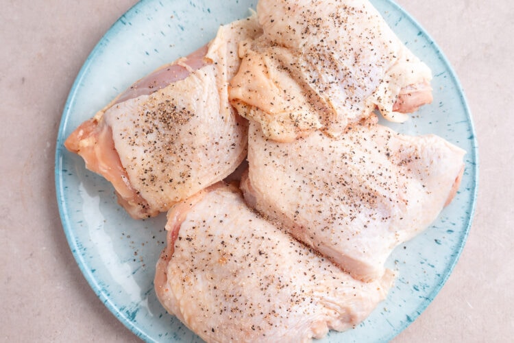 Chicken thighs seasoned with salt and pepper on a large round plate.