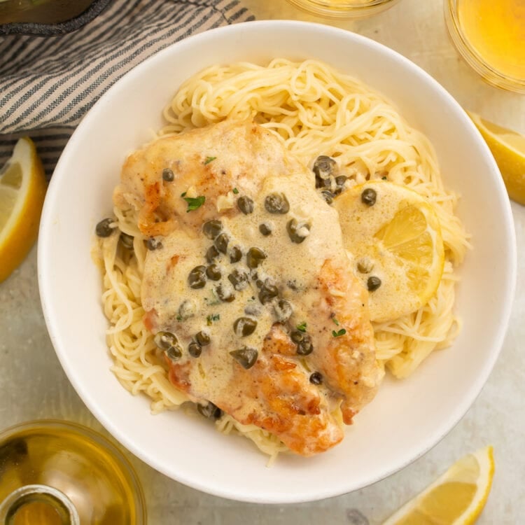 Creamy chicken piccata on a round white plate with lots of lemon sauce and capers.