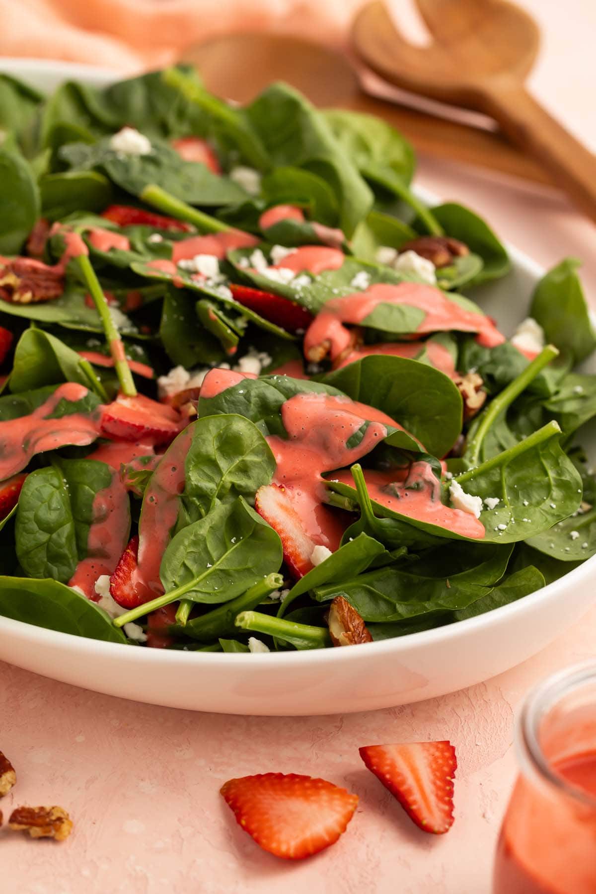 Pale red strawberry vinaigrette drizzled over a leafy green spinach salad in a bowl on a table.