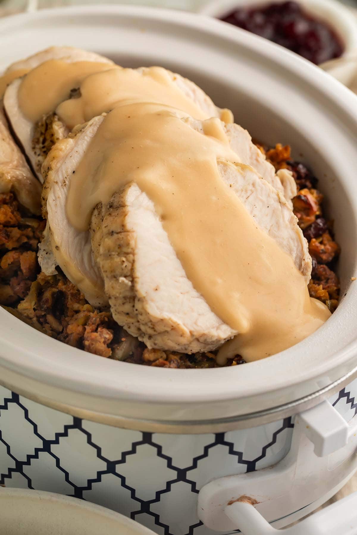 Close-up of thick slices of turkey, smothered in gravy, on top of cooked stuffing and green beans in a Crockpot.