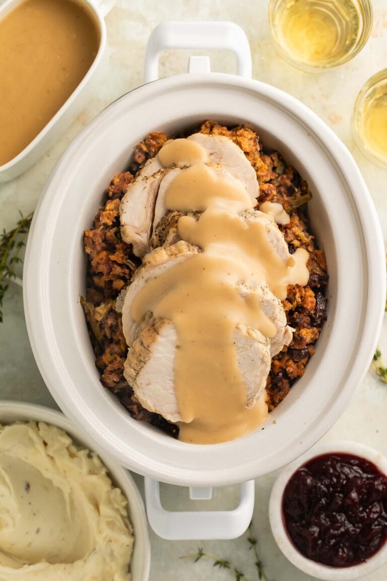 Overhead view of thick slices of turkey, smothered in gravy, on top of cooked stuffing and green beans in a Crockpot.