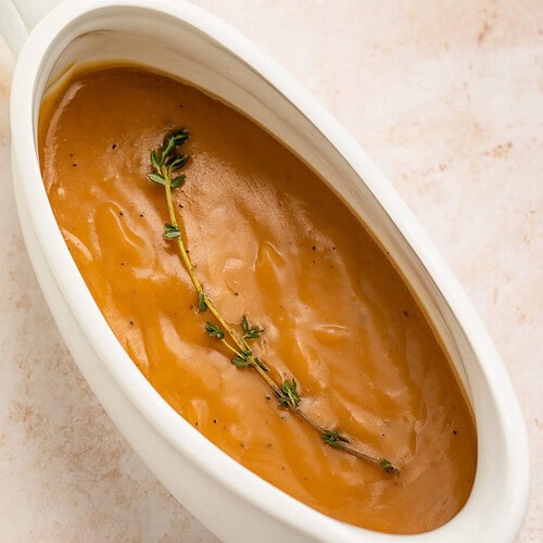 White gravy boat of gravy topped with a single fresh thyme sprig.