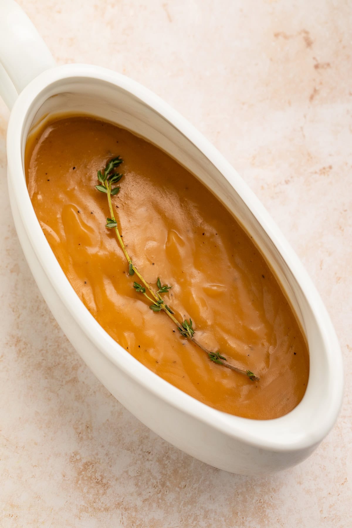 White gravy boat of gravy topped with a single fresh thyme sprig.