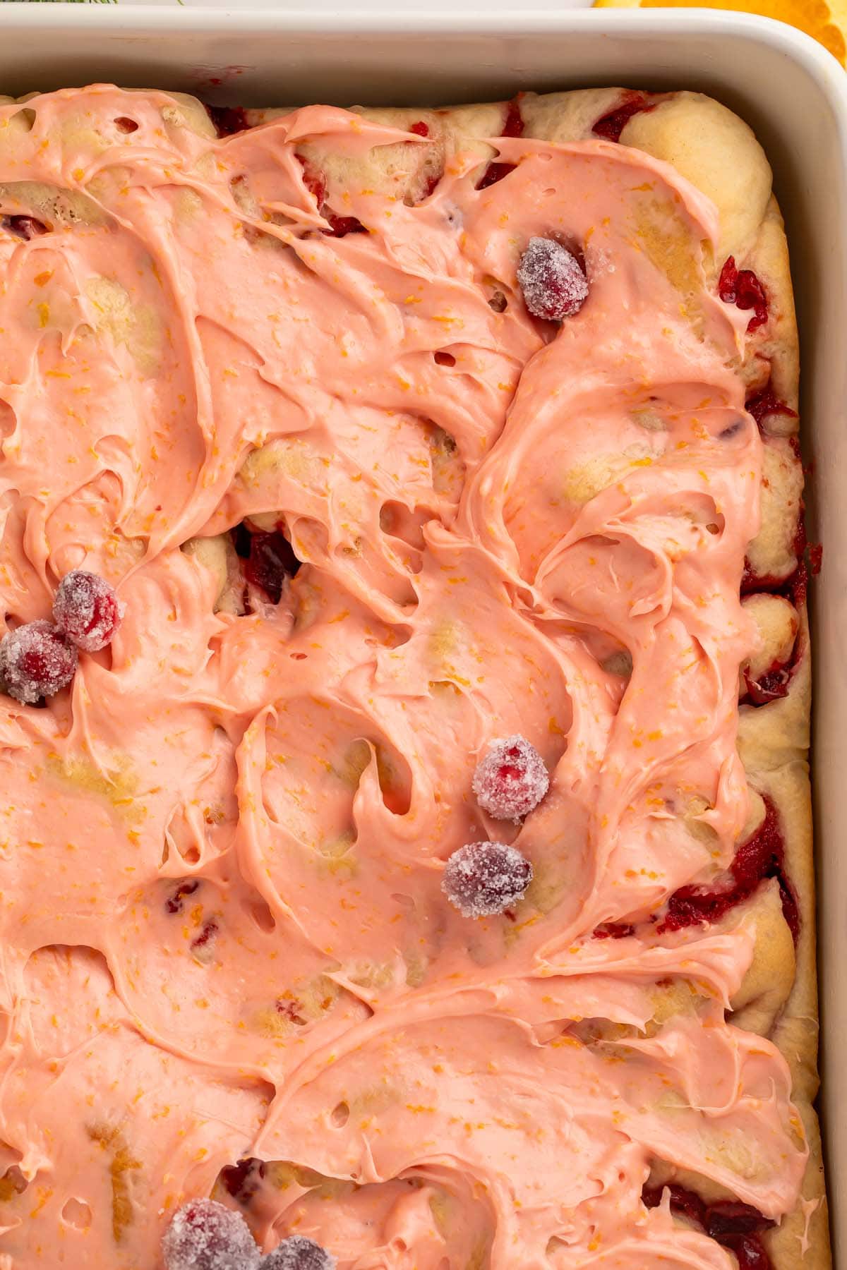 The upper right corner of a full pan of cranberry cinnamon rolls topped with pink frosting.