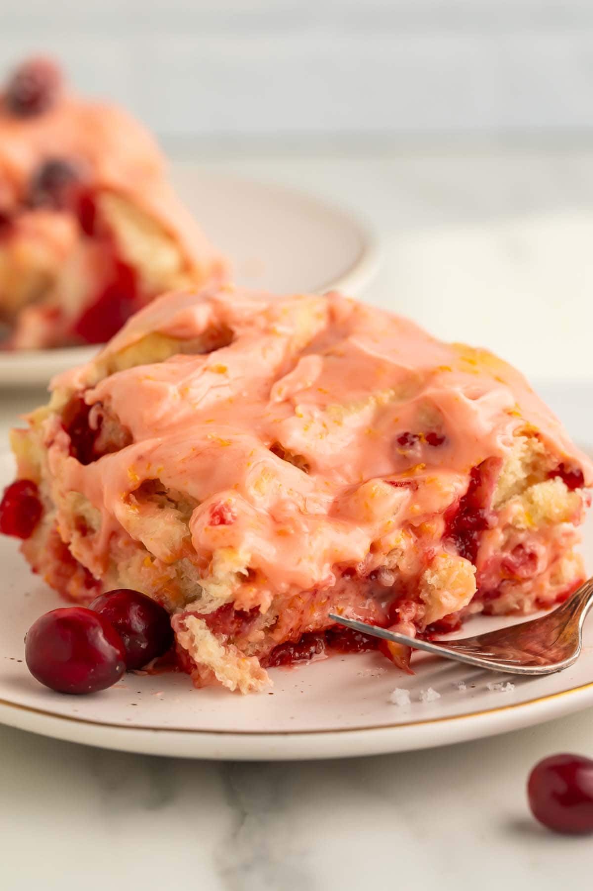 A cranberry orange cinnamon roll resting on a small plate with 2 loose cranberries.