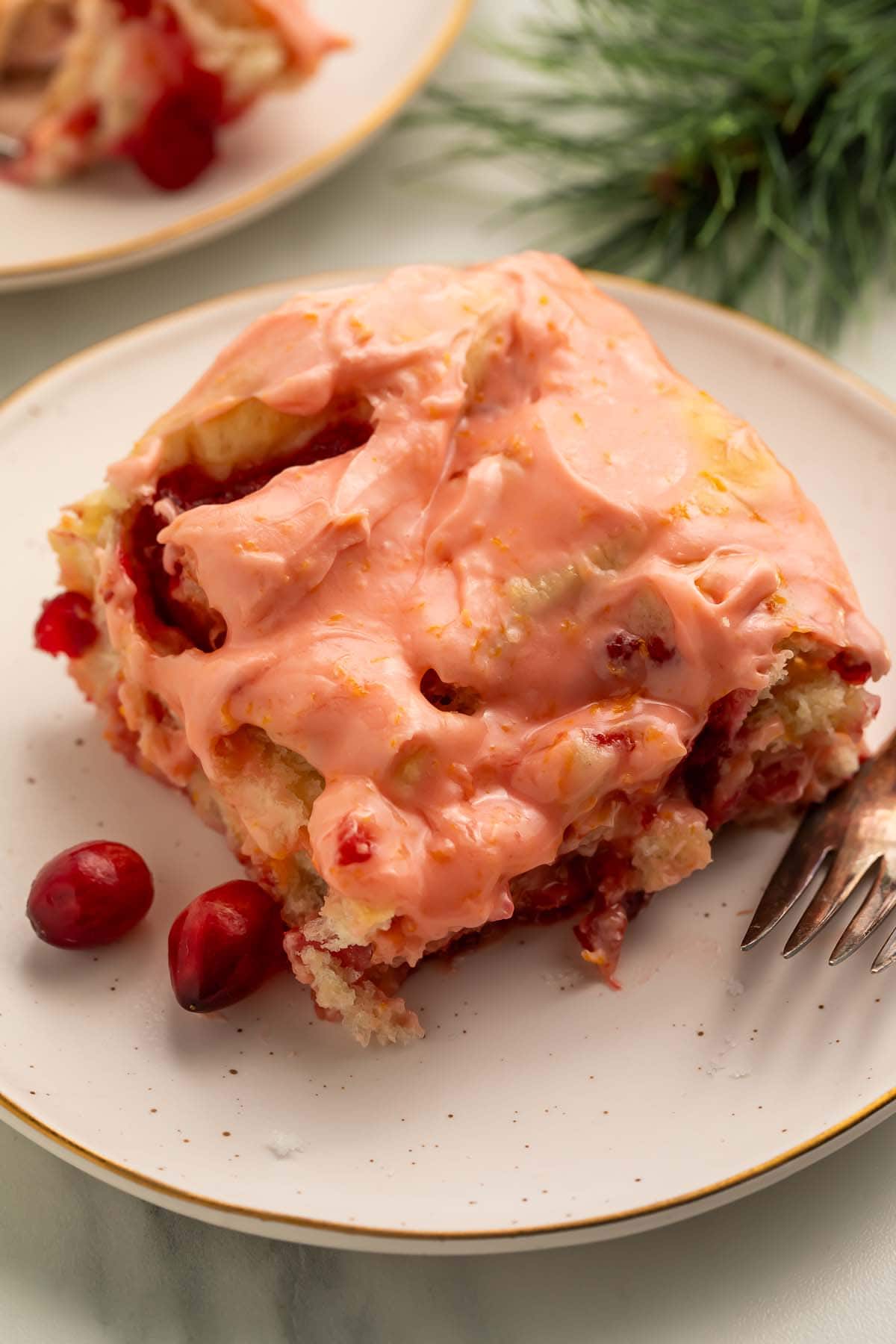 A cranberry orange cinnamon roll resting on a small plate with 2 loose cranberries.