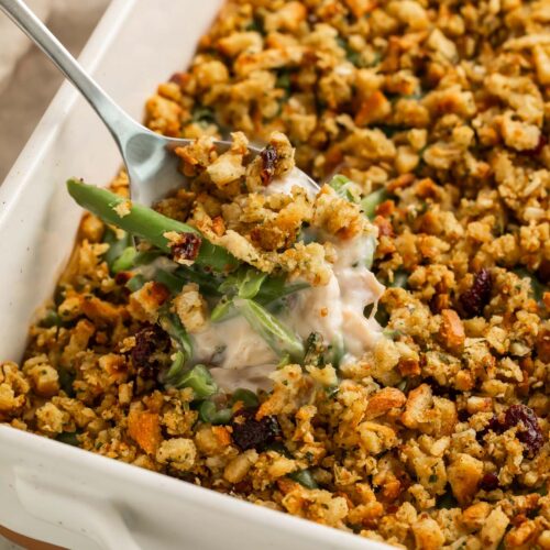 A scoop of creamy chicken and stuffing casserole being lifted out of a casserole dish, showing the creamy sauce and green beans inside.