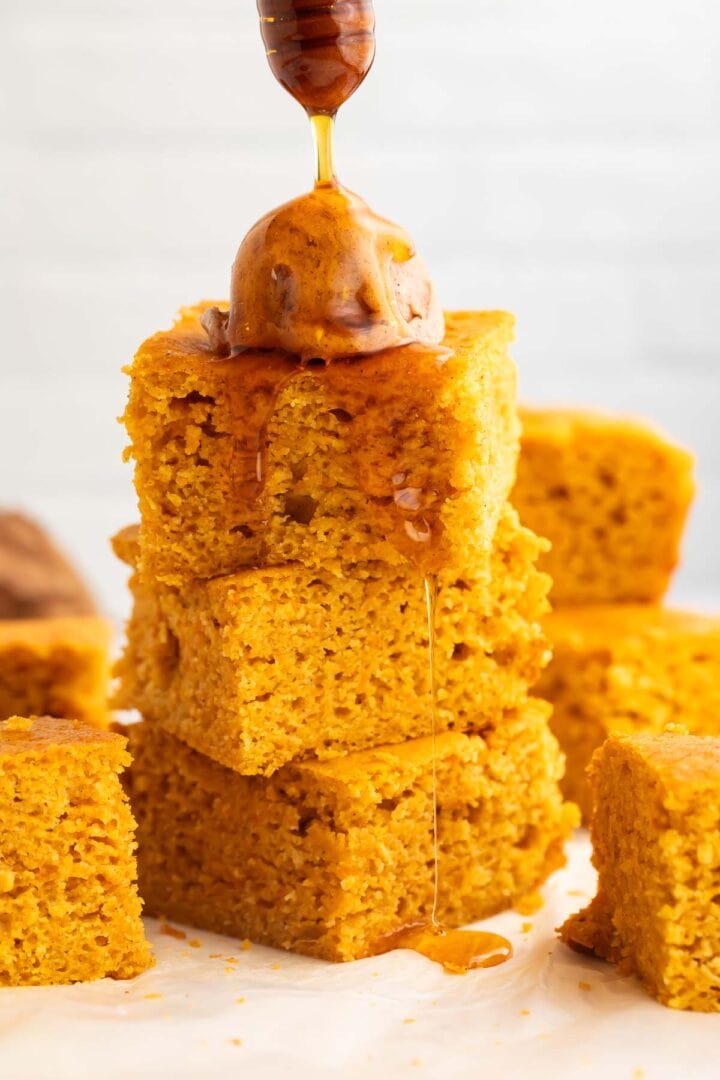 Honey being drizzled over a stack of sweet potato cornbread squares topped with a scoop of cinnamon honey butter.