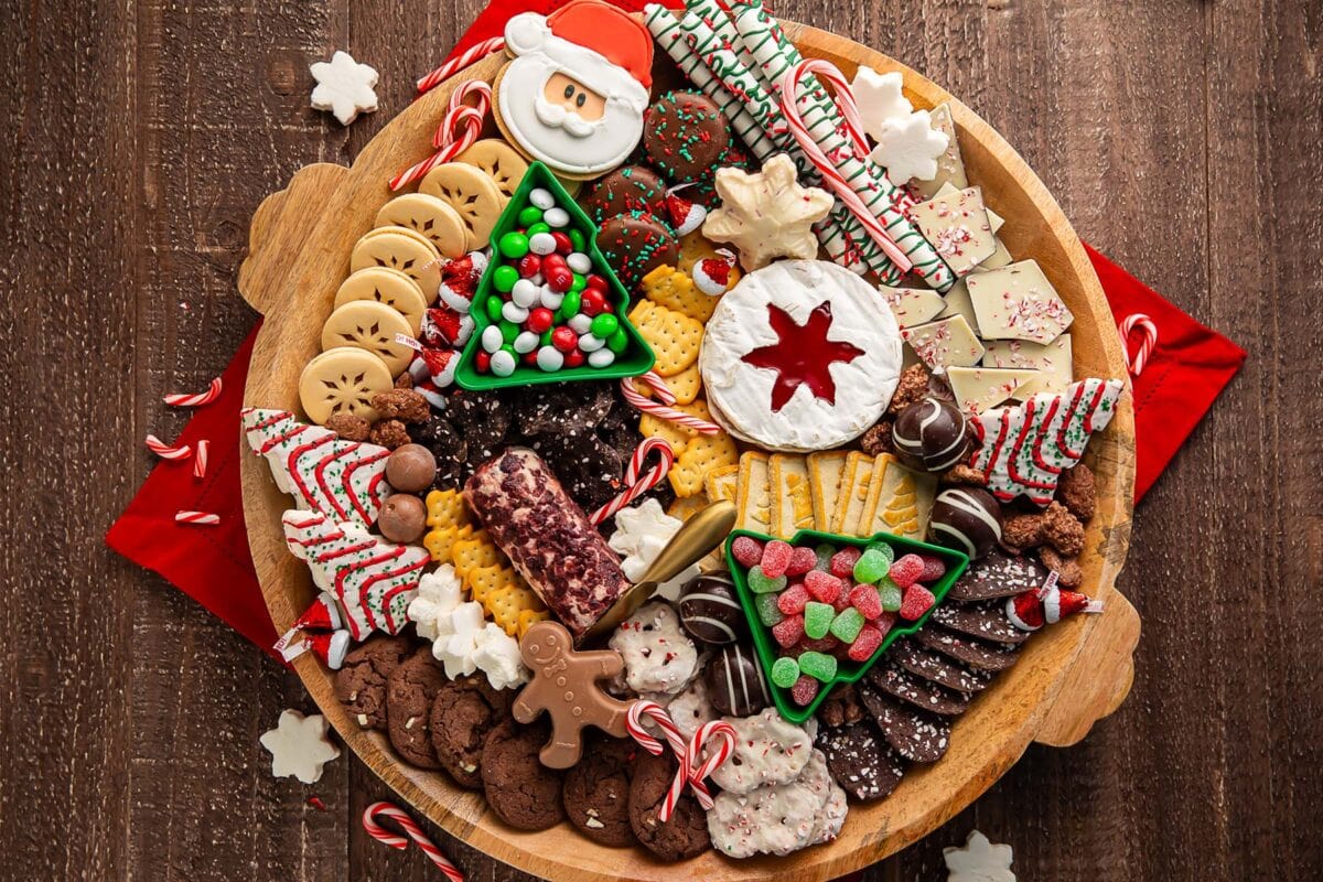 A Christmas dessert themed grazing board, packed full with Christmas tree cakes, brie, goat cheese, crackers, pretzels, truffles, nuts, cookies, and other holiday-themed treats.