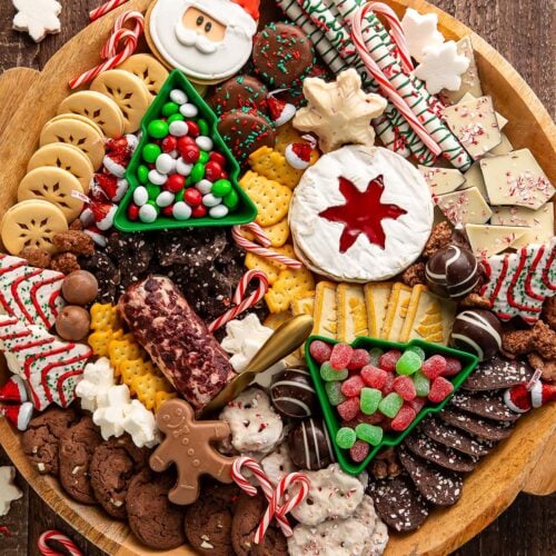 A Christmas dessert themed grazing board, packed full with Christmas tree cakes, brie, goat cheese, crackers, pretzels, truffles, nuts, cookies, and other holiday-themed treats.