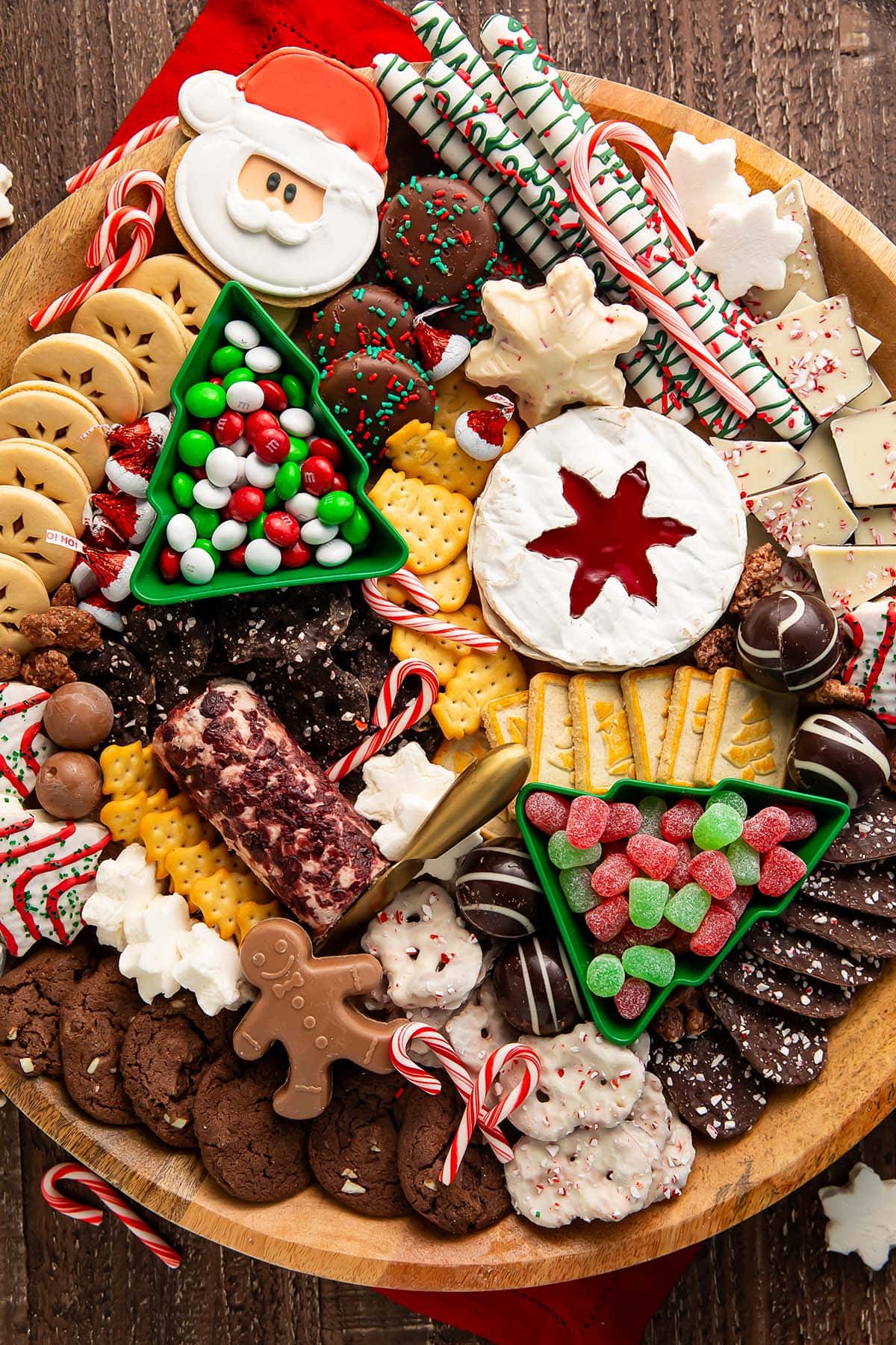 A Christmas dessert themed grazing board, packed full with Christmas tree cakes, brie, goat cheese, crackers, pretzels, truffles, nuts, cookies, and other holiday-themed treats.