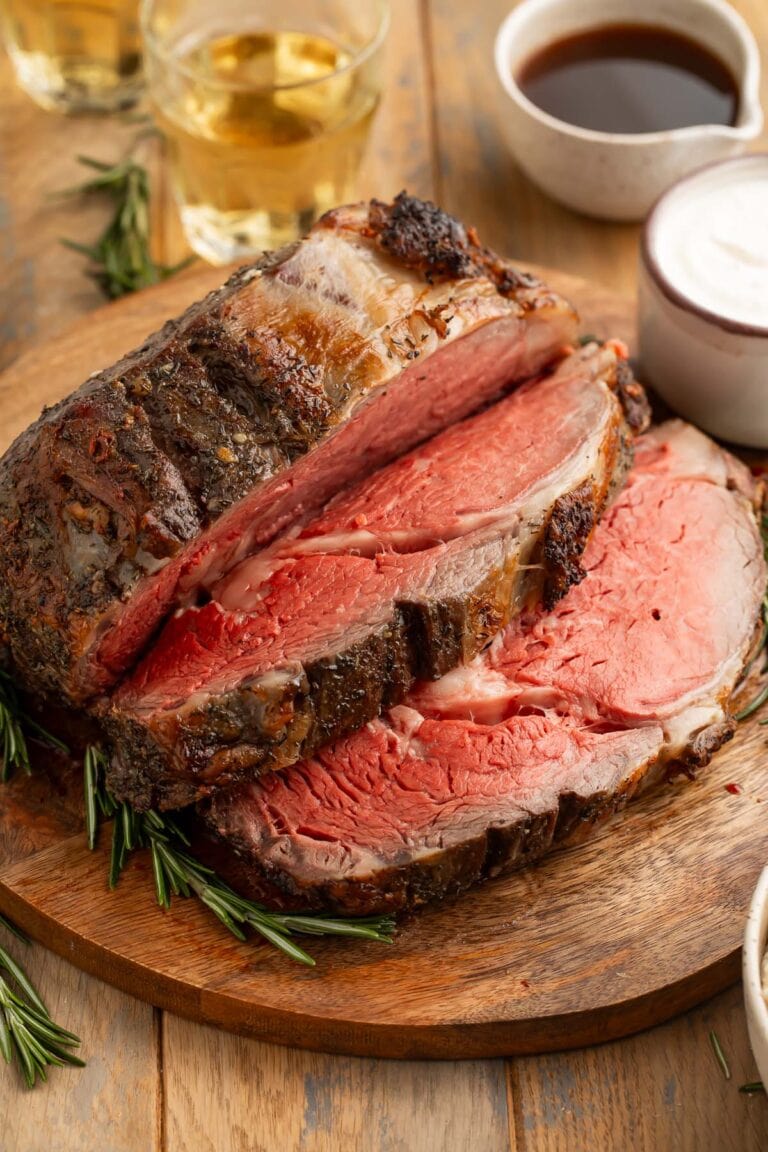 A thickly-carved reverse sear prime rib on a wooden cutting board next to prepared horseradish sauce and au jus.