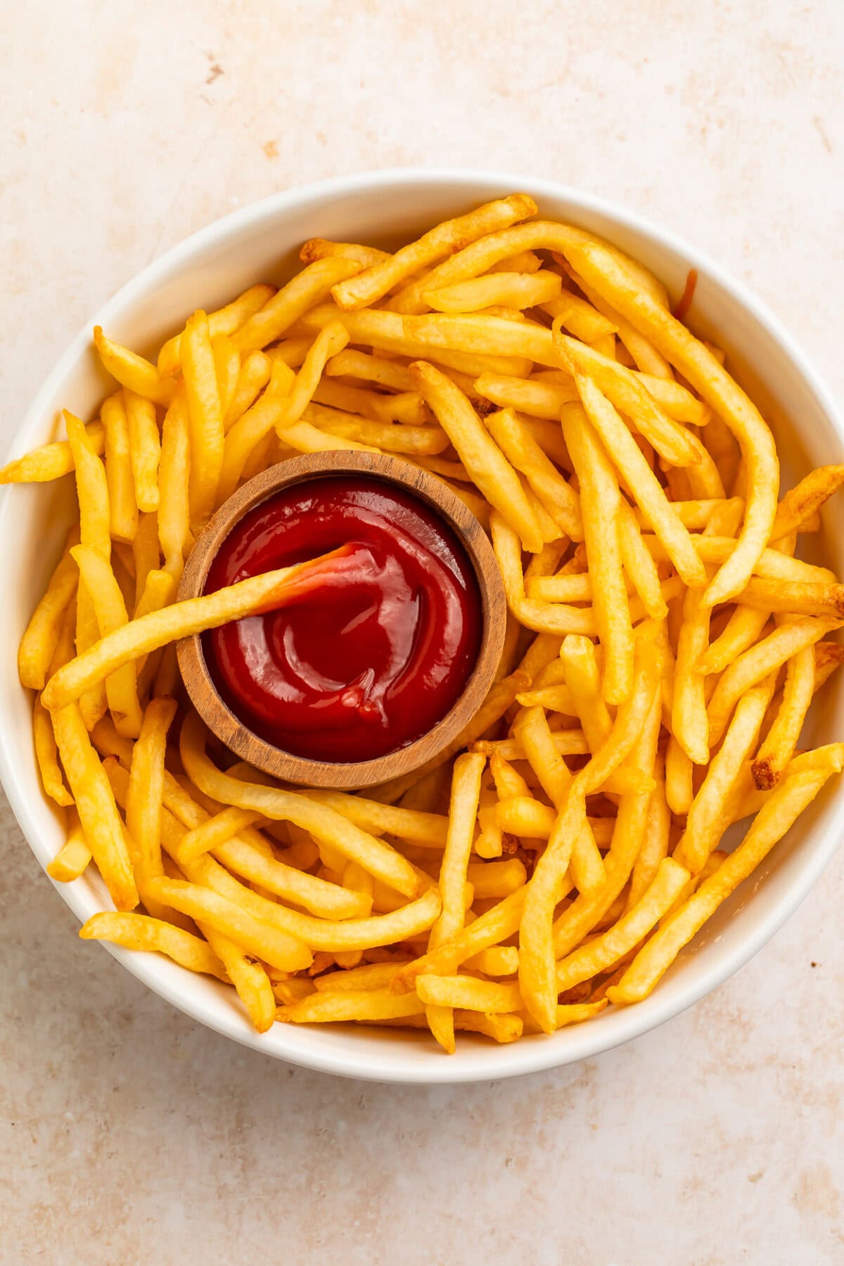 Overhead view of golden french fries on a white plate with ketchup in center.