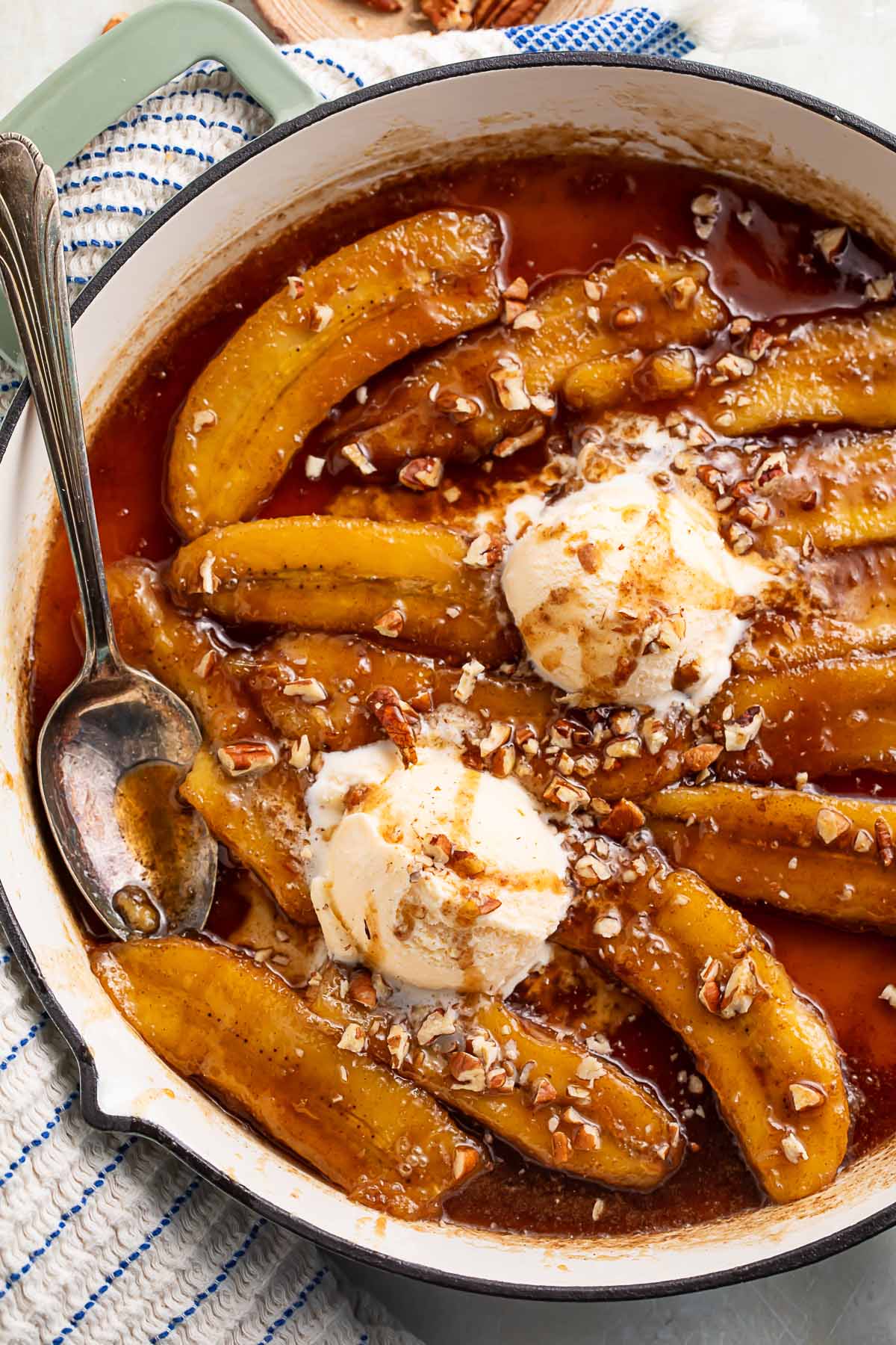 Rich bananas foster topped with scoops of vanilla ice cream in a large pan.