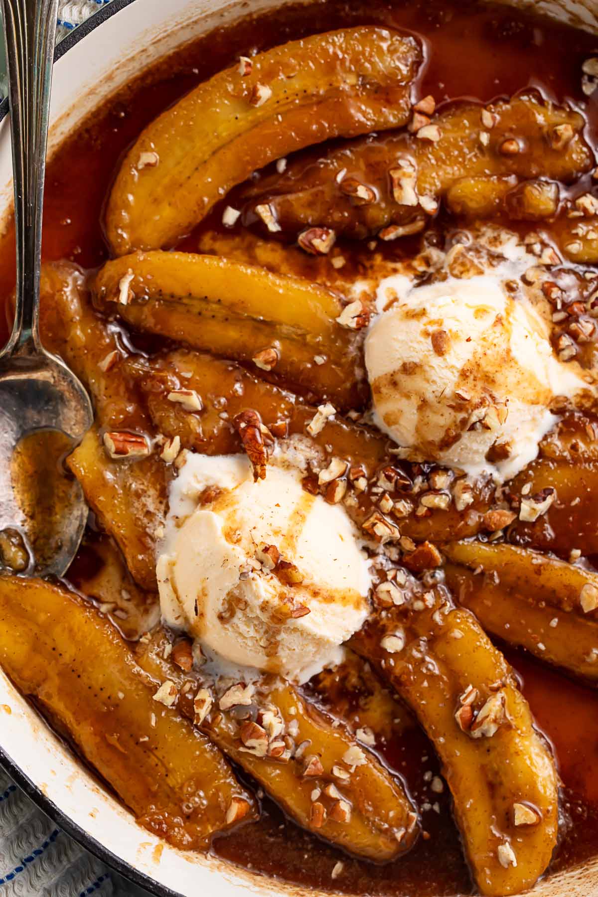 Rich bananas foster topped with scoops of vanilla ice cream in a large pan.