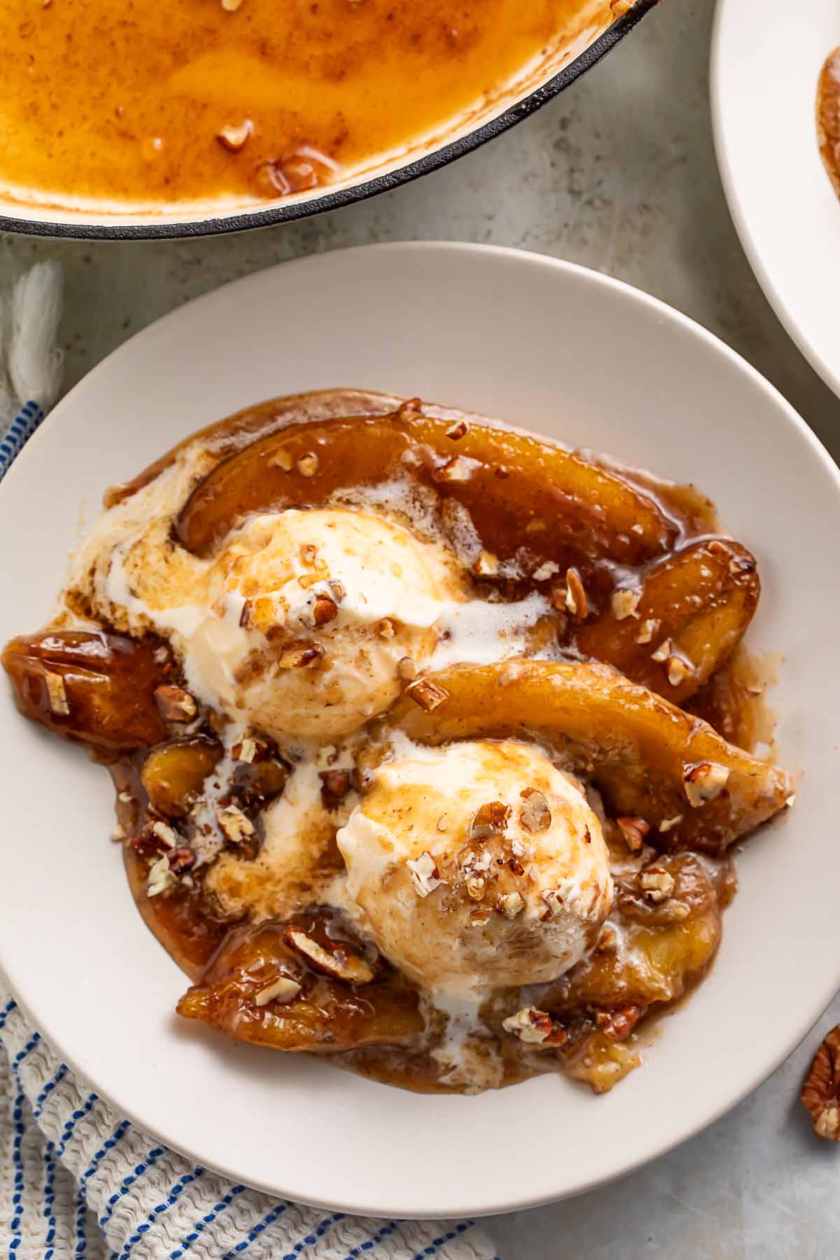 Bananas foster over scoops of vanilla ice cream and topped with chopped pecans in a large bowl.