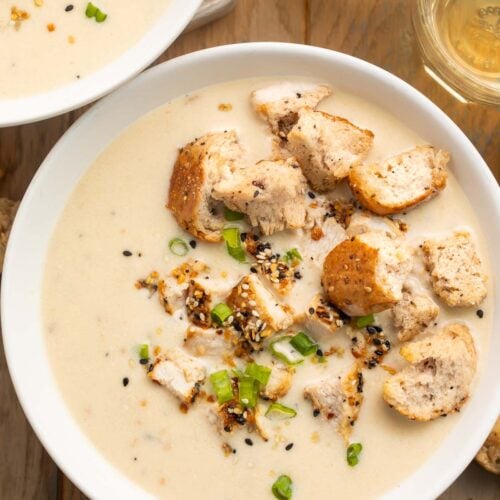 Overhead photo of a bowl of thick, creamy everything bagel chicken soup, topped with sliced green onions and homemade everything bagel croutons.