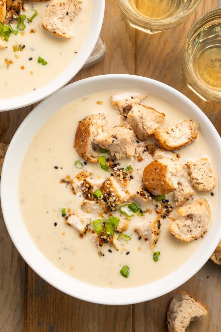 Overhead photo of a bowl of thick, creamy everything bagel chicken soup, topped with sliced green onions and homemade everything bagel croutons.